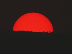 Tinted blood red by a thick cloud of smoke and pollution, the sun sets on the mountains above Mexico City, Monday, May 13, 2019. Mexico City's government has warned residents to remain indoors as forest and brush fires carpeted the metropolis in a smoky haze that has alarmed even many of those accustomed to living with air pollution.