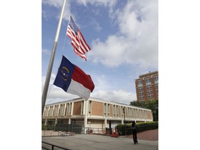 A man rides a scooter past flags at half staff at the University of North Carolina-Charlotte in Charlotte, N.C., Wednesday, May 1, 2019. A student with a pistol and no apparent motive killed two people and wounded four others Tuesday evening before campus police disarmed and arrested him.
