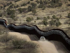 FILE - This March 2, 2019 photo shows a Customs and Border Control agent patrols on the US side of a razor-wire-covered border wall along the Mexico east of Nogales, Ariz.  A surge of asylum-seeking families that has strained cities along the southern U.S. border for months is now being felt in cities far from Mexico. Immigrants are being housed in airplane hangars and rodeo fairgrounds, while local authorities are struggling to keep up with the influx.
