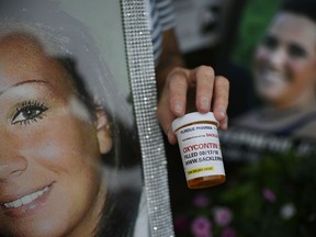 FILE - In this Friday, Aug. 17, 2018, file photo, a demonstrator holds a prescription drug bottle with a mock label to protest Purdue Pharma and its product, OxyContin, outside the company's headquarters in Stamford, Conn. The protest was organized by those who have lost loved ones in the opioid epidemic.