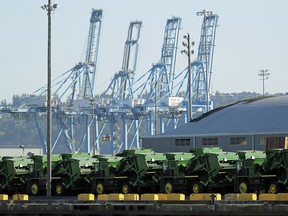 FILE - In this May 10, 2019, file photo John Deere Agricultural machinery made by Deere & Company sits staged for transport near cranes at the Port of Tacoma in Tacoma, Wash. Deere's fiscal second-quarter earnings were a mixed bag and the agricultural equipment maker lowered its full-year outlook as the trade war between the U.S. and China intensifies and conditions in the agricultural sector soften.