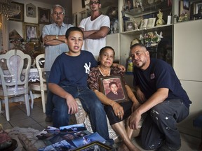 FILE - In this July 24, 2014, file photo, while holding a favorite childhood portrait of her late son Rolando Perez, Carmen Perez, 65, center, is joined by her husband Pedro Perez, 65, rear left, their other sons Ricardo Perez, 41, rear right, Pedro Perez, 45, right, and their grandson Rolando Perez, Jr., 13, second from left, at home in the Bronx borough of New York. New York City has reached a $3.5 million settlement in a lawsuit filed over the 2014 death of Rolando Perez, a Rikers Island inmate who records show was deprived of seizure medication. The New York Daily News reports the city agreed last week to pay the money to the girlfriend of Rolando Perez, mother of his now-18-year-old son.