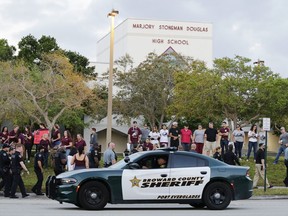 FILE - In this Feb. 28, 2018 file photo, a police car drives near Marjory Stoneman Douglas High School in Parkland, Fla., as students return to class for the first time since a former student opened fire there with an assault weapon. Republican Florida Gov. Ron DeSantis has signed a bill that will allow more classroom teachers to carry guns in school, a response to last year's mass shooting at a Parkland high school.