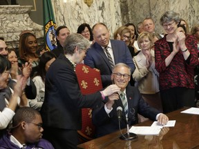 Gov. Jay Inslee, seated, hands Democratic Rep. Laurie Jinkins his pen after he signed a measure that makes Washington the first state in the nation to establish a program to help offset the costs of long-term care, Monday, May 13, 2019, in Olympia, Wash. Starting in 2025, the program promises a benefit for those who pay into the program, with a lifetime maximum of $36,500 per person, indexed to inflation, paid for by an employee payroll premium.