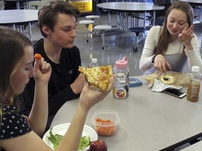 In this Friday, April 5, 2019 photo, Burlington High School student Emma McCobb, left, holds a piece of pizza while eating with classmates in the school cafeteria in Burlington, Vt. The school's food service provider is preparing to comply with a Trump administration decision to roll back a rule that required only whole-grain rich foods for school meals. Burlington officials said they don't plan on abandoning whole-grain foods, but it gives them flexibility.