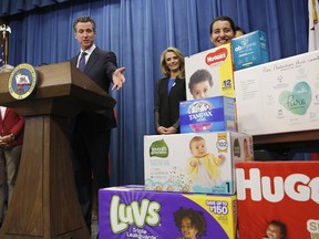 Gov. Gavin Newsom gestures towards boxes of tampons and diapers after proposing to eliminate from the state sales tax on such products in his upcoming state budget during a news conference, Tuesday, May 7, 2019, in Sacramento, Calif. The tax cuts are part of a "parents' agenda" Newsom is pursuing, and he plans to unveil a revised state budget later this week. Newsom was, accompanied by his wife, first partner Jennifer Siebel Newsom, center, Southern California Democratic Assemblywoman Monique Limon, right, and others.