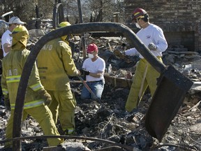 FILE - In this Nov. 17, 2008 file photo, firefighters from Santa Ana Engine No. 4 help Lindy Lindholm, center, sift through the rubble of his burned out home in Yorba Linda, Calif. A group of public and private water systems in California have launched an advertising and lobbying campaign aimed at convincing lawmakers to shield them from having to pay damages caused by fires they did not start but failed to help put out. One lawsuit stemming from the 2008 fire forced the Yorba Linda Water District to pay $70 million to 12 homeowners.