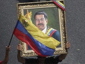 In this May 1, 2019 photo, supporters of Venezuelan President Nicolas Maduro carry a portrait of him during a rally in Caracas, Venezuela.