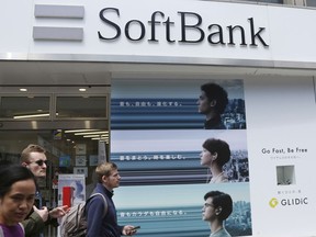 In this April 15, 2019, photo, people walk under the logo of Japanese telecoms company Softbank Corp. at its mobile phone shop in Tokyo. Softbank said Wednesday, May 8, 209, it will spend 456.5 billion yen ($4 billion) to increase its stake in Yahoo Japan to nearly 45%. The company forecast that with the additional stake in Yahoo, its revenue will rise to 4.8 trillion yen ($43.6 billion) in this fiscal year.