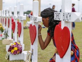 FILE - In a Monday, May 21, 2018 file photo, Santa Fe High School freshman, Jai Gillard writes messages on each of the 10 crosses representing victims in front the school in Santa Fe, Texas. Texas, which for years has buckled to pressure from the National Rifle Association, has quietly gone around the organization by slipping a $1 million public safety campaign on gun storage into a massive spending bill now headed to Republican Gov. Greg Abbott's desk.