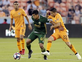 Portland Timbers midfielder Renzo Zambrano (40) moves the ball between Houston Dynamo forward Mauro Manotas (9) and midfielder Matias Vera (22) during the first half of an MLS soccer match Wednesday, May 15, 2019, in Houston.