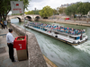 A man watches a tourist barge cruises past as he stands at a “uritrottoir” public urinal on the Saint-Louis island in Paris.
