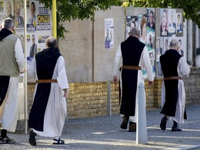 Monks from the Saint Sixtus Trappist Abbey walk by election campaign posters as they walk to a polling station in Westvleteren, Belgium, Sunday, May 26, 2019. Belgium, which has one of the oldest compulsory voting systems, goes to the polls Sunday to vote on the regional, federal and European level.