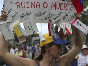 An opponent of the Nicolas Maduro government holds up a homemade poster from which hang empty boxes of medication with a message that reads in Spanish: "Ruin or death" as she waits for the arrival of opposition leader Juan Guaidó to lead a rally in Caracas, Venezuela, Saturday, May 11, 2019. Guaidó has called for nationwide marches protesting the Maduro government, demanding new elections and the release of jailed opposition lawmakers.