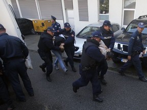 FILE - In this Sunday, Oct. 16, 2016 file photo, Montenegrin police officers escort people suspected of planning armed attacks after the parliamentary vote in Podgorica, Montenegro. A court in Montenegro has sentenced 13 people, including two Russian secret service operatives, to up to 15 years in prison after they were found guilty of plotting to overthrow the Balkan country's government and prevent it from joining NATO.