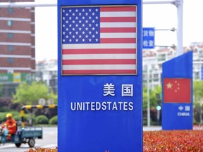 In this Wednesday, May 8, 2019, photo, a worker drives an electric cart past a display featuring the U.S. and Chinese flags in a special trade zone in Qingdao in eastern China's Shandong province. China said Thursday it will retaliate if President Donald Trump goes ahead with more tariff hikes in a fight over technology and trade, ratcheting up tensions ahead of negotiations in Washington. (Chinatopix via AP)