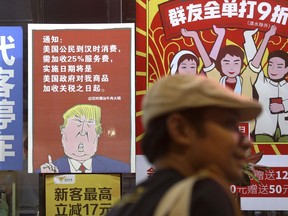 FILE - In this Aug. 13, 2018, file photo, a man walks by a poster depicting a mural of U.S. President Donald Trump stating that all American costumers will be charged 25 percent more than others starting from the day president Trump started the trade war against China, on display outside a restaurant in Guangzhou in south China's Guangdong province. What do tilapia, Jane Austen and revolutionary posters have in common? All have been used in recent days to rally public support around China's position in its trade dispute with the U.S., as the ruling Communist Party takes a newly aggressive approach to controlling the narrative and stirring up nationalistic sentiment. (Color China Photo via AP, File)