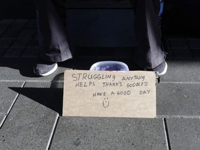 A man sits with a bowl asking for money in the central business district of Christchurch, New Zealand, Thursday, May 30, 2019. The liberal-led government on Thursday unveiled the country's first so-called well-being budget, which aims to measure social outcomes like health and the environment alongside traditional metrics such as economic growth.