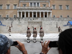 Red paint is seen on the wall of the Parliament building as Greek Presidential Guards, changing of the guard at the tomb of the unknown Soldier in Athens, Tuesday, May 21, 2019. A group of about 10 people threw red paint at parliament and set off a smoke bomb as Greece's Supreme Court is hearing an appeal against the denial of a temporary leave of absence from prison of a hunger striking extremist serving multiple life sentences for the killings of 11 people by the country's deadliest far-left group.