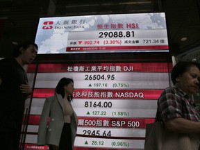 People walk past a bank electronic board showing the Hong Kong share index at Hong Kong Stock Exchange Monday, May 6, 2019.  Shares tumbled in Asia early Monday after President Donald Trump threatened in a tweet to impose more tariffs on China, spooking investors who had been expecting good news on trade.