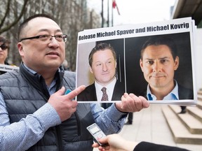 In this file photo taken on March 6, 2019, Louis Huang of Vancouver Freedom and Democracy for China holds photos of Canadians Michael Spavor and Michael Kovrig, who are being detained by China, in Vancouver.