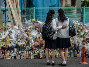 A schoolgirl comforts her friend as they pause next to flowers and tributes laid at the scene of a knife attack on a group of schoolchildren, on May 29, 2019 in Kawasaki, Japan.