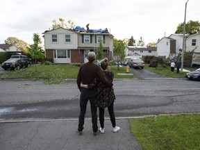 Dominik Lesniewski and Catherine O'Sullivan look at their home from across the street as roofers put tarps over damage to their roof caused by a tornado in the Ottawa suburb of Orleans, Sunday, June 2, 2019.