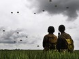 Men dressed as American soldiers watch paratroopers from Britain's 16 Air Assault Brigade and France's 11th Parachute Brigade perform a jump over Sannerville, north-western France, on June 5, 2019, prior to D-Day commemorations marking the 75th anniversary of the World War II Allied landings in Normandy.