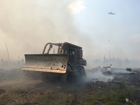 A bulldozer clears debris as crews battle a forest fire near Pikangikum First Nation, Ont. in this undated handout photo. The chief of an Ontario First Nation threatened by a forest fire says a plan to evacuate residents via buses and boats today has been paused because of a lack of space in host communities.