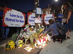 People place flowers and candles at a makeshift memorial remembering the victims of a shooting on Sunday evening on Danforth, Ave. in Toronto on Monday, July 23, 2018. The doors at St. Barnabas on the Danforth are always open, but the people seeking solace inside the Anglican church the day after a deadly shooting wanted to bolt them shut.