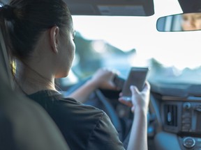 A woman looks at her phone while driving. A French motorist can have their license confiscated if caught with their phone behind the wheel, authorities say