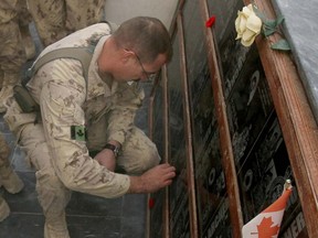 A soldier places a poppy on a plaque during the cenotaph Remembrance Day ceremonies at Kandahar Air Field.