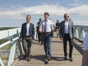 Prime Minister Justin Trudeau, center, walks across a pedestrian bridge next to the St.John River in downtown Fredericton with Member of Parliament for Fredericton, Matt DeCourcey, left, and Mayor of Fredericton, Mike O'Brien in Fredericton, New Brunswick on Thursday August 15, 2019. Trudeau was in Fredericton to discuss federal funding for flood mitigation.