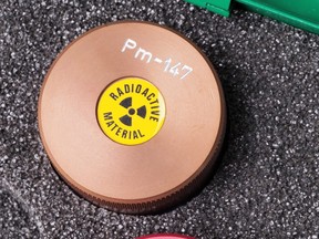 A specialist container with warning sticker and engraving containing radioactive isotope Promethium 147 in a box.