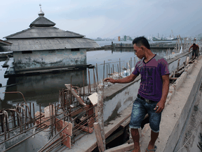 A workman inspects a seawall being rebuilt behind an abandoned mosque which has been surrounded by the encroaching sea in the Maura Baru district in Jakarta, Indonesia.  Jakarta, Southeast Asia's largest city is sinking slowly into the sea, largely due to overconsumption of ground water.