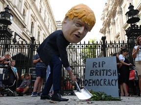 A demonstrator, wearing a mask depicting Britain's Prime Minister Boris Johnson, and a mock gravestone inscribed with the words "RIP British Democracy" protests outside the gates to Downing Street in central London on August 28, 2019.
