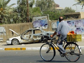 An Iraqi man rides a bicycle passing by the remains of a car in Baghdad on Sept. 20, 2007. The car was burned during an incident in which Blackwater guards escorting U.S. embassy officials opened fire in a Baghdad neighbourhood, four days earlier.
