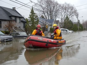 Firefighters make their way through a flooded street on Friday, May 3, 2019 in Ste-Marthe-sur-la-Lac, Quebec. Lakeside residents of a small town north of Montreal that was severely flooded last spring after a dike ruptured are now upset the government's repairs to the structure will obstruct their view of the water.