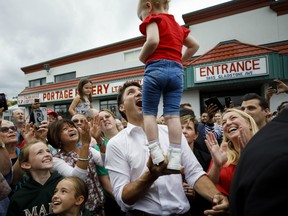 Prime Minister Justin Trudeau balances a toddler alongside local Liberal candidate Andrea Kaiser, during a campaign stop in Niagara Falls on Sept. 23, 2019.