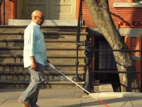 A man walks down a street with a white WeWalk smart cane in hand.