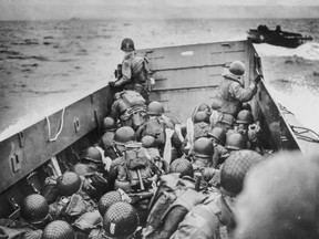 Soldiers crouch behind the bulwarks of a Coast Guard landing barge on their way to Normandy.