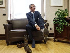 Alberta Finance Minister Travis Toews puts on a pair of cowboy boots during a pre-budget photo op in Edmonton on Wednesday, Oct. 23, 2019.