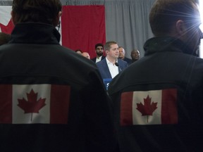 Conservative staff members wearing jackets with the Canadian flag on them look on as Conservative leader Andrew Scheer addresses the media during a morning announcement during a campaign stop in Toronto Friday, October 4, 2019.