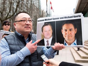 In this file photo taken on March 6, 2019, Louis Huang of Vancouver Freedom and Democracy for China holds photos of Canadians Michael Spavor and Michael Kovrig, who are being detained by China, in Vancouve, Canada - Canada on May 16 2019,  demanded that China promptly release Spavor and Kovrig, who were formally arrested following months of detention on national security grounds, amid rising tensions between the two nations.