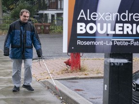 Jerome Plante, who is visually impaired, walks along a sidewalk towards a low-hanging election sign in Montreal on Tuesday, October 1, 2019. An advocacy group for the visually impaired is calling out political parties for their low-hanging Montreal election signs that create a hazard for those unable to see them.