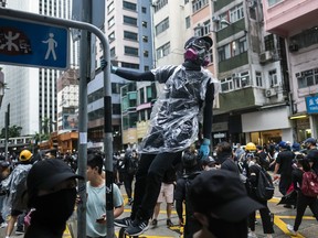 A demonstrator wearing a gas mask holds on to a signpost during a protest on Queens Road East in the Wan Chai district of Hong Kong, China, on Sunday, Oct. 6, 2019. Violence escalated in Hong Kong as protesters set fires and vandalized train stations and banks, pushing back against government efforts to quell demonstrations when it invoked a colonial-era emergency law.