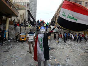 An Iraqi demonstrator wearing a Guy Fawkes mask in reverse and draped in a national flag waves another national flag before others celebrating the resignation of Prime Minister Adel Abdul-Mahdi's government, during a demonstration along Rasheed Street in the centre of the capital Baghdad, on November 29, 2019.