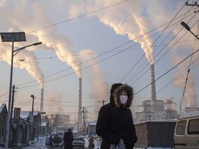 Smoke billows from stacks as a woman wears a mask while walking in a neighbourhood next to a coal fired power plant in Shanxi, China.