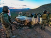 People stand near the burned car where part of the nine murdered members of the family were killed and burned during an ambush in Bavispe, Sonora mountains, Mexico, Nov. 5, 2019.