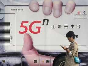 A woman using her mobile phone walks past a vehicle covered in a China Unicom 5G advertisement in Beijing, China September 17, 2019.